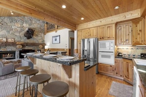 Una cocina con armarios de madera, pared de piedra, chimenea de piedra y una isla grande con taburetes.