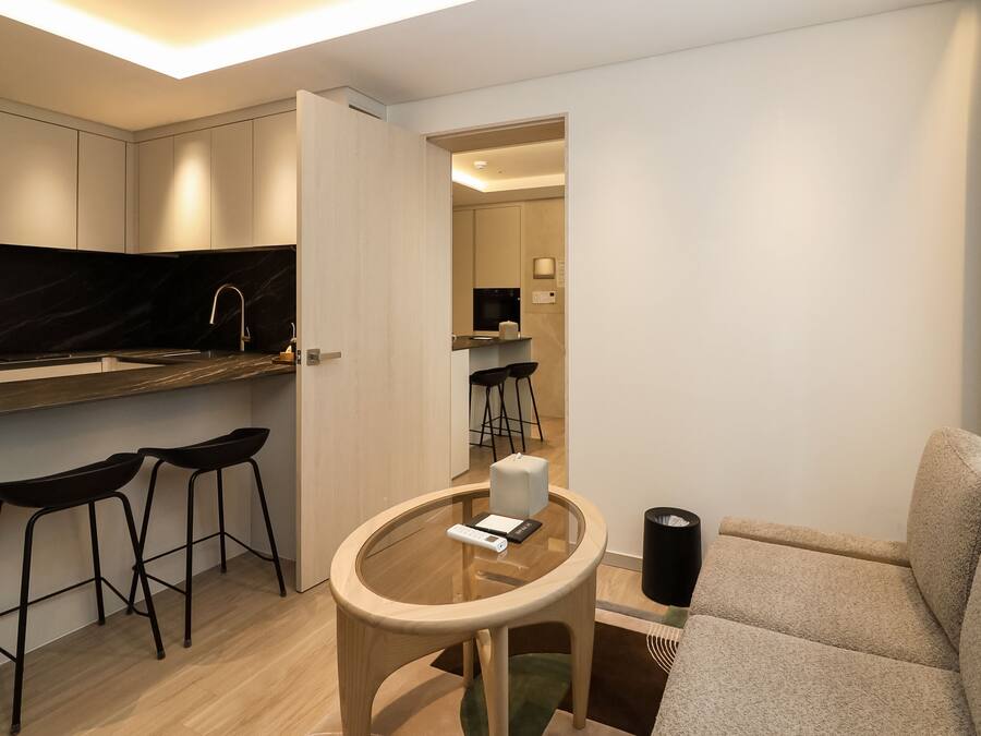 A modern kitchen with a marble backsplash, a dining area with a glass table and black stools, and a living area with a sofa and a coffee table.