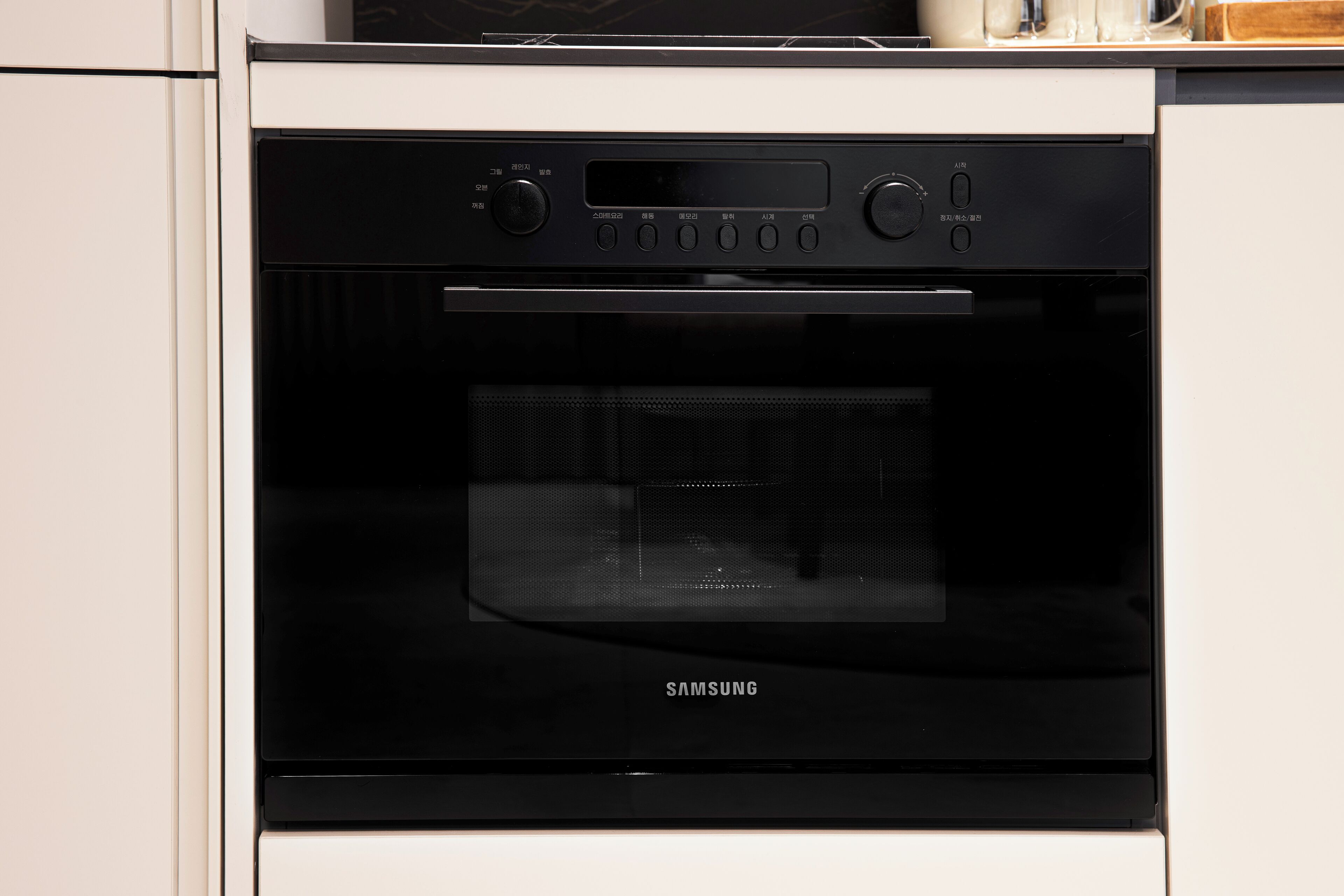 A Samsung oven with a digital display and control panel, installed in a kitchen with white cabinetry.