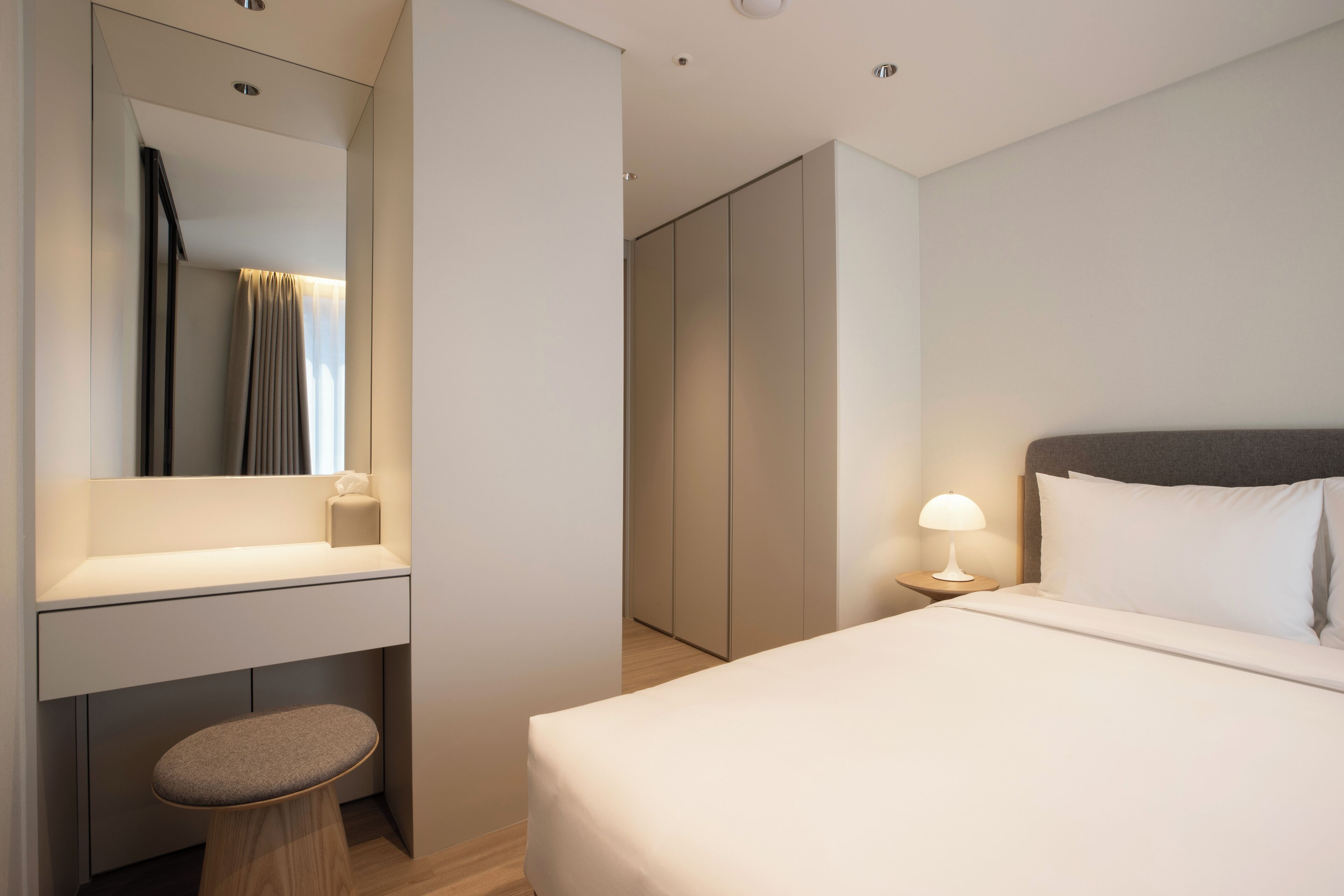 Ett modernt hotellrum med en säng, ett skrivbord, en stol, en spegel och en garderob.