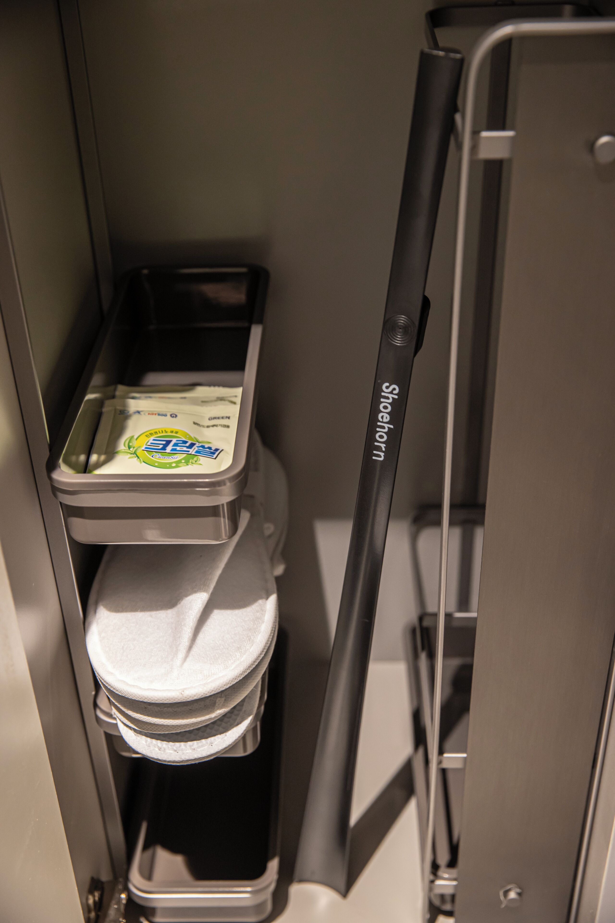 A compact bathroom with a toilet, a trash bin, and a shoehorn.