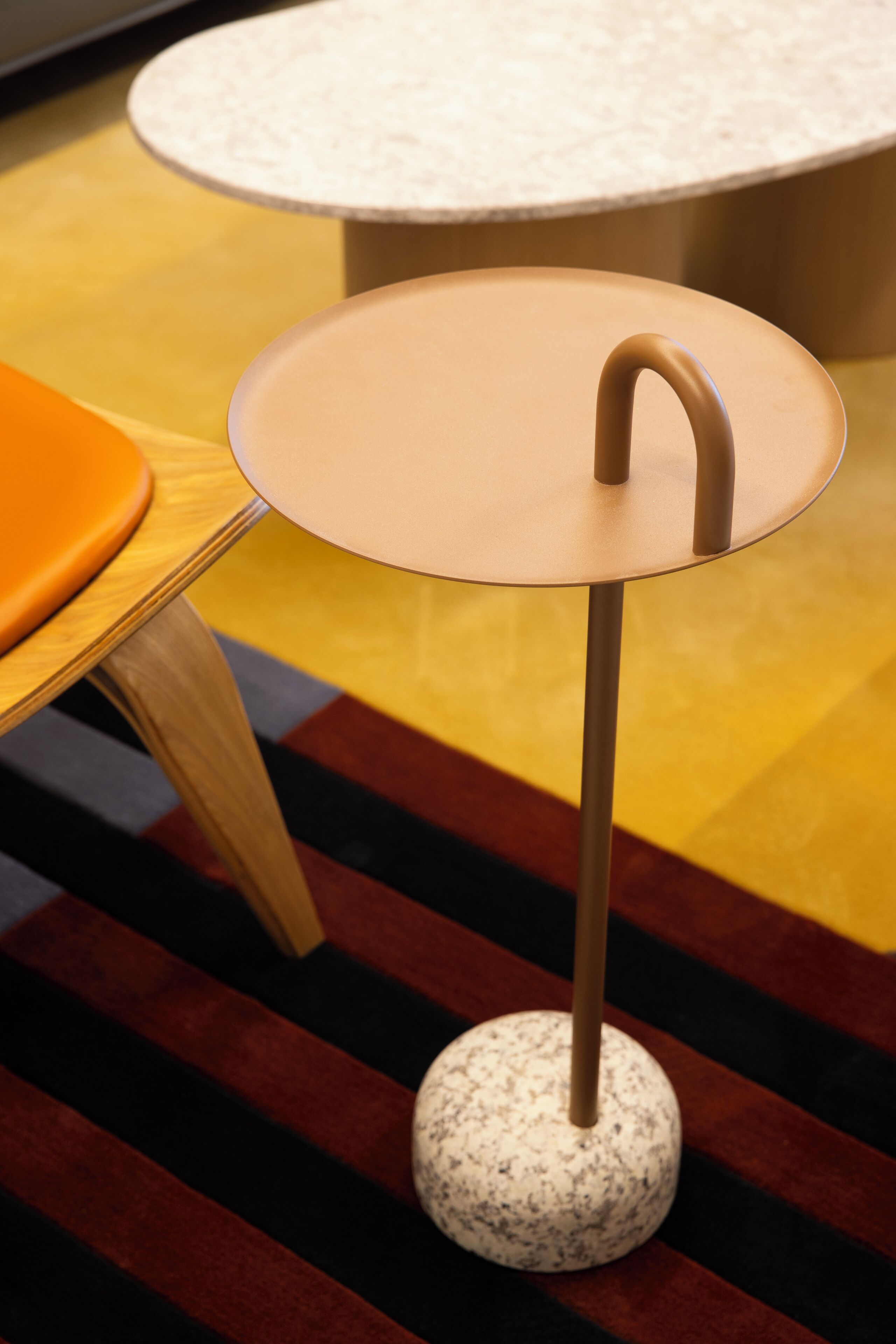 A round table with a curved leg and a white top, placed on a multicolored striped carpet.