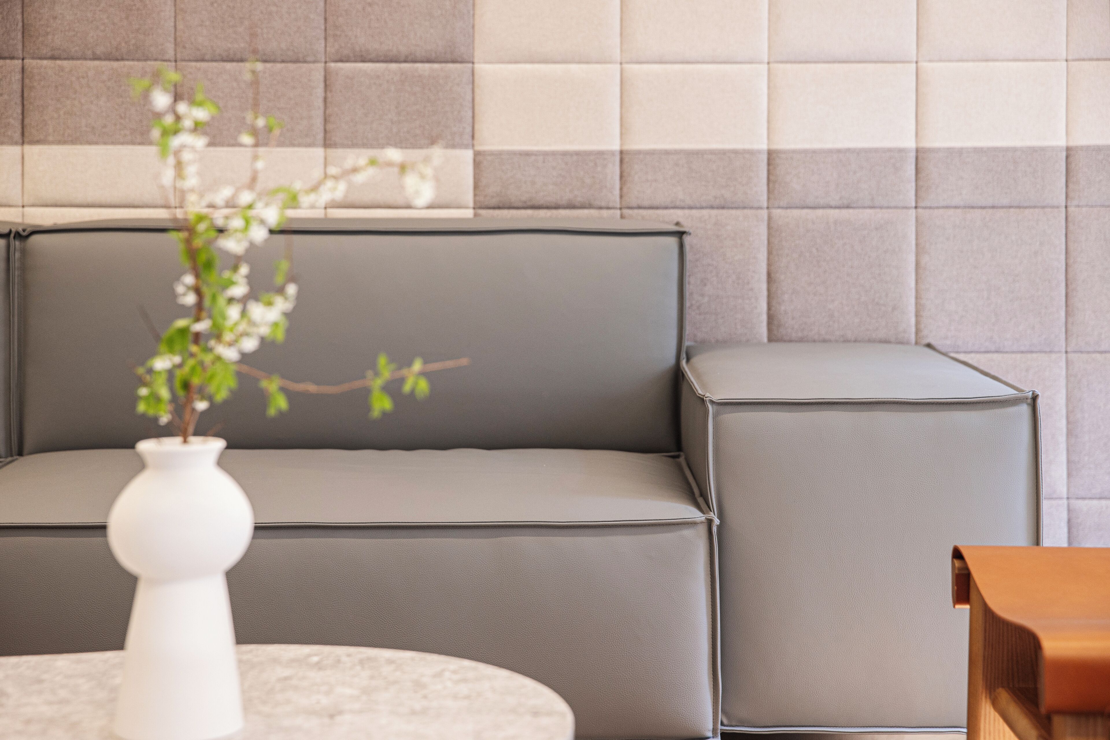 A modern living room with a grey sofa, a white vase with a plant, and a wooden side table.