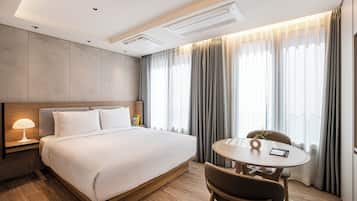 A modern hotel room with a large bed, bedside table, lamp, and a round table with chairs.