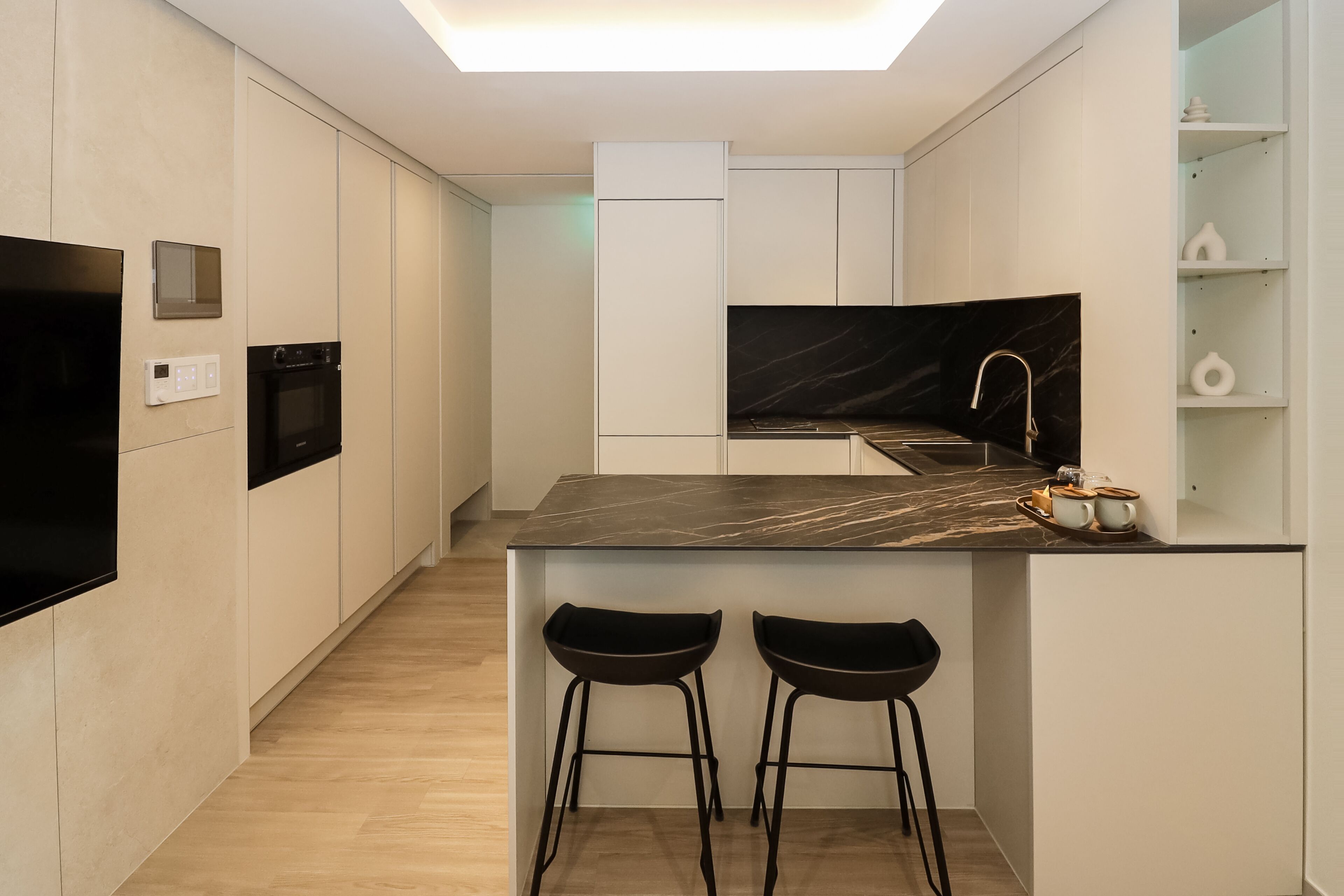 Una cocina moderna con encimera de mármol negro, dos taburetes negros, horno empotrado y una elegante salpicadera.