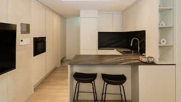 Una cocina moderna con encimera de mármol negro, dos taburetes negros, horno empotrado y una elegante salpicadera.