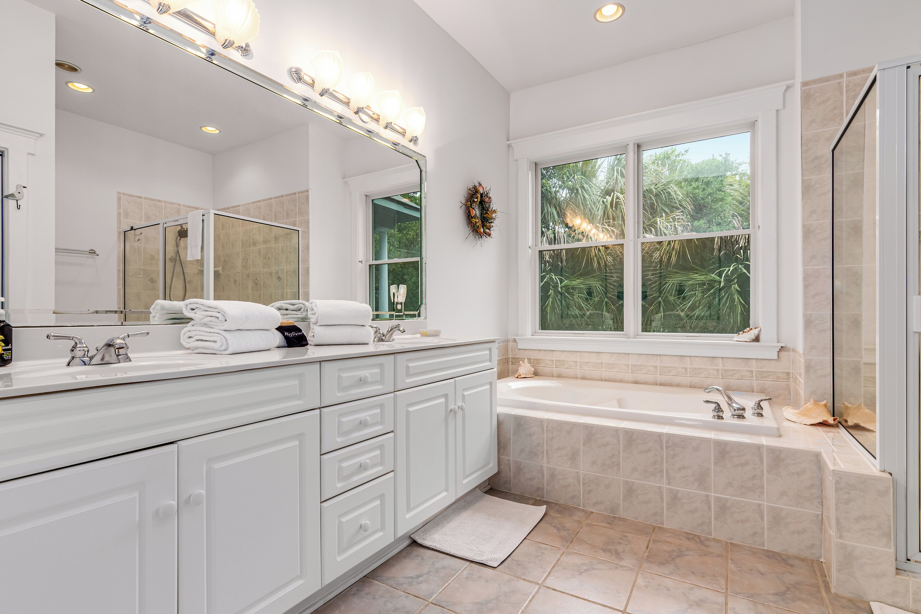 A modern bathroom with a large mirror, white vanity, and a bathtub.
