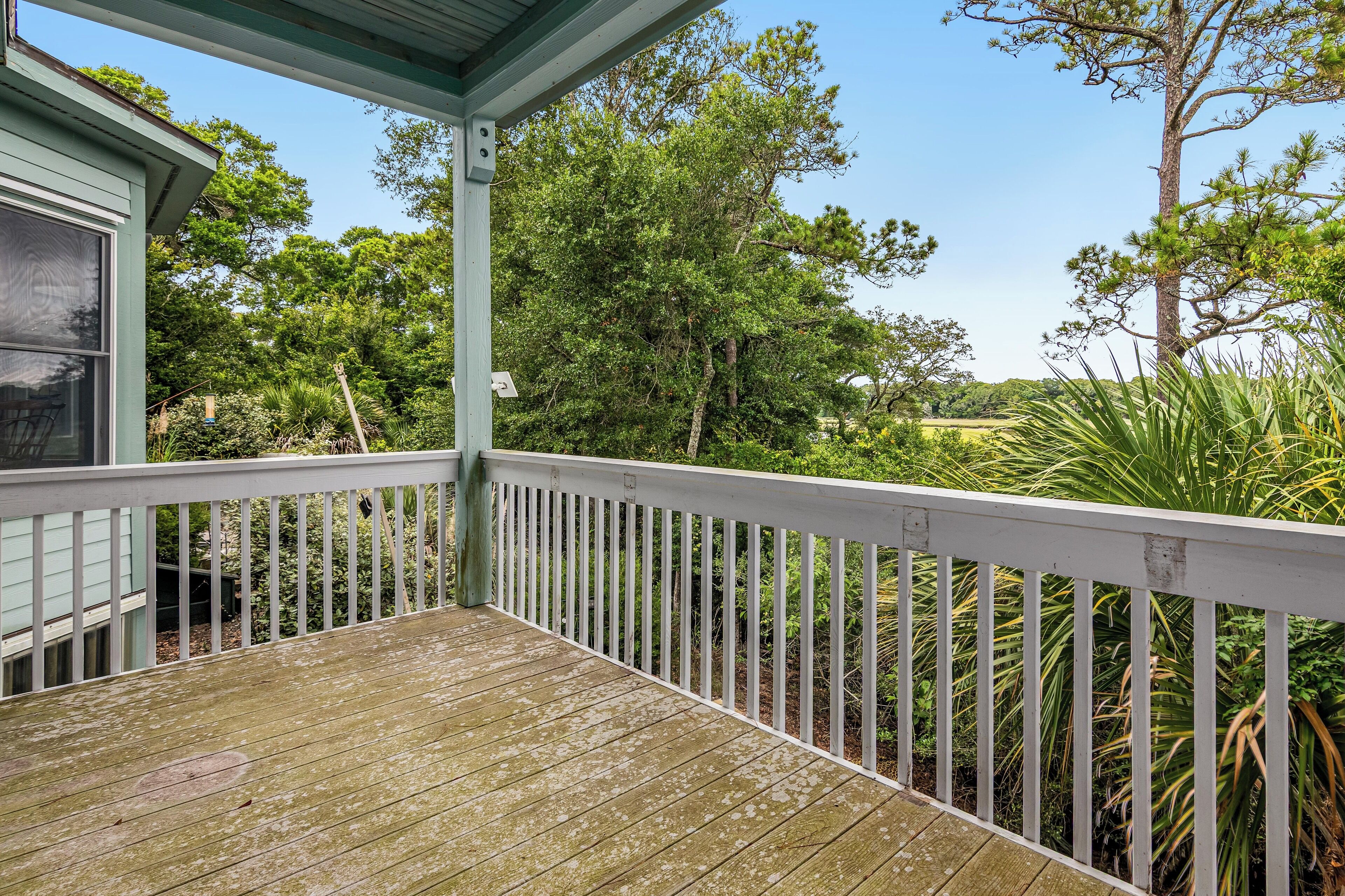 A wooden deck with a white railing, overlooking a lush garden with various trees and plants.