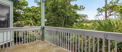 A wooden deck with a white railing, overlooking a lush garden with various trees and plants.
