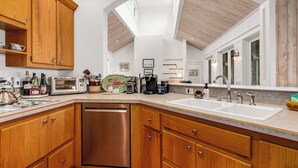Una cocina moderna con armarios de madera, lavavajillas, pileta doble y un amplio ventanal que proporciona luz natural.