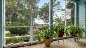 Una terraza de madera con plantas en macetas y un ventanal con vistas a un jardín.