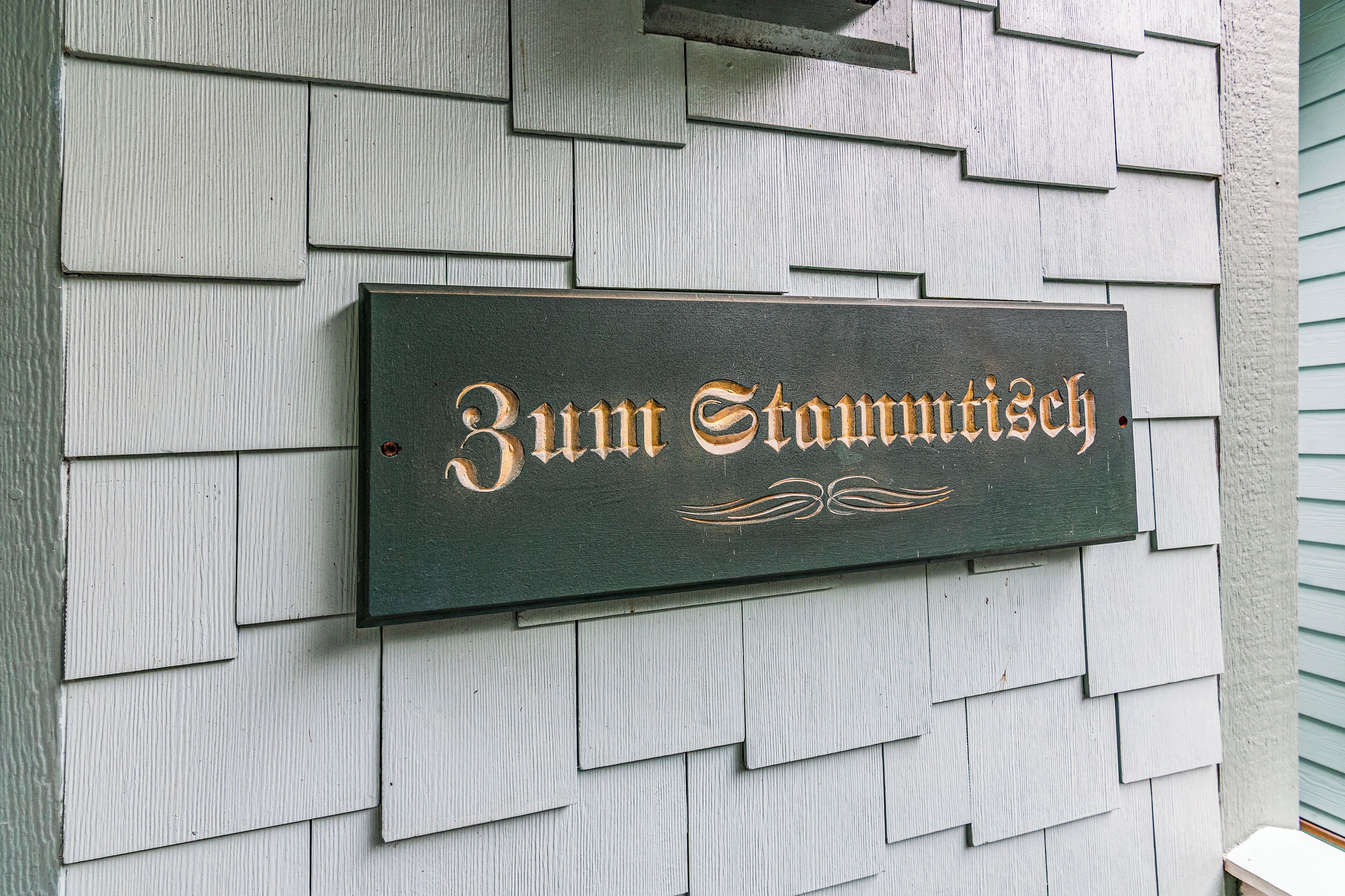 A wooden sign with the text "Zum Stamtisch" mounted on a wall with shingle siding.