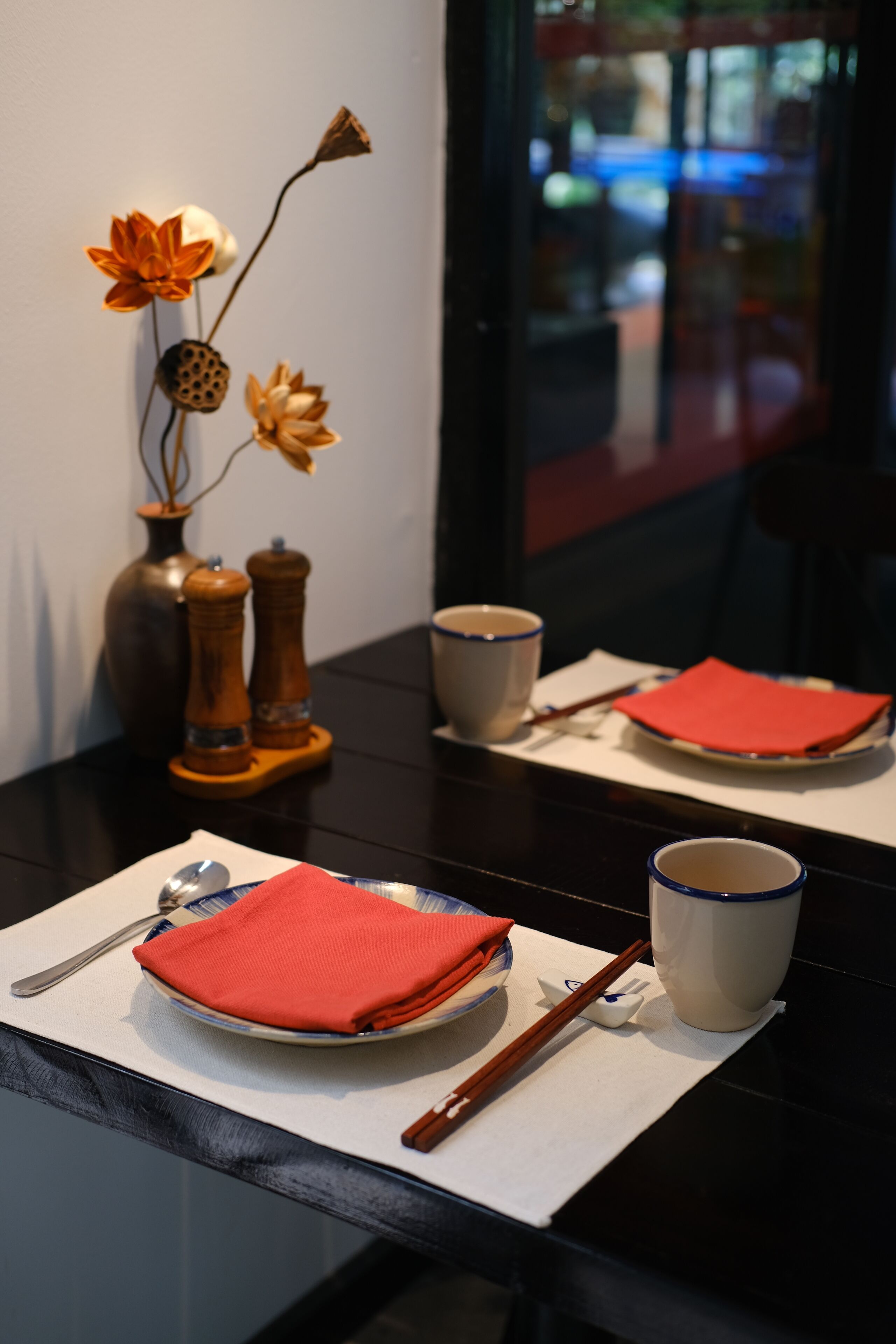 A dining table with a vase, salt and pepper shakers, chopsticks, a plate with a napkin, and a cup.