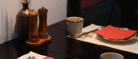 A dining table with a vase, salt and pepper shakers, chopsticks, a plate with a napkin, and a cup.