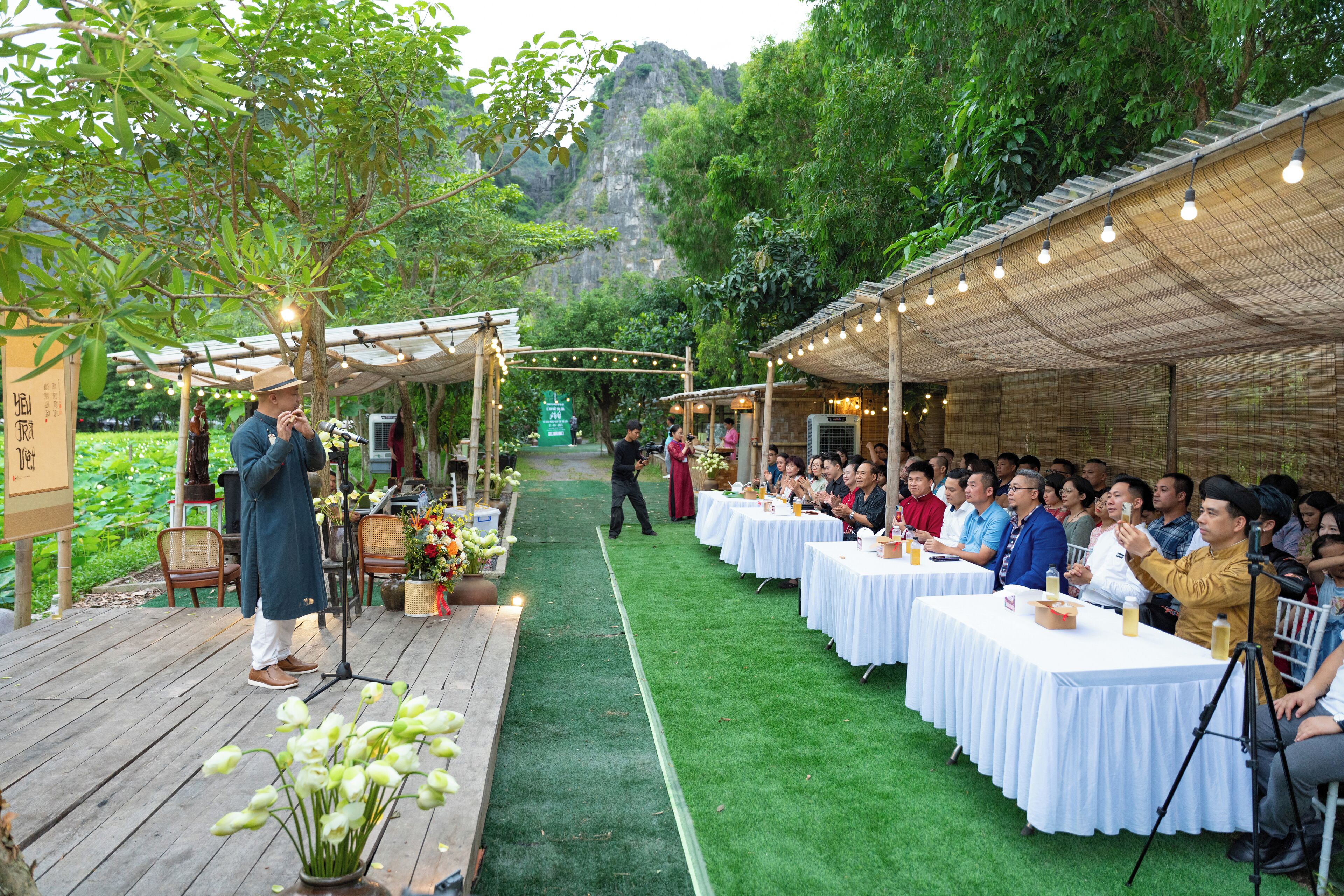 An outdoor event with a stage, audience, and tables set up under a covered area with string lights.