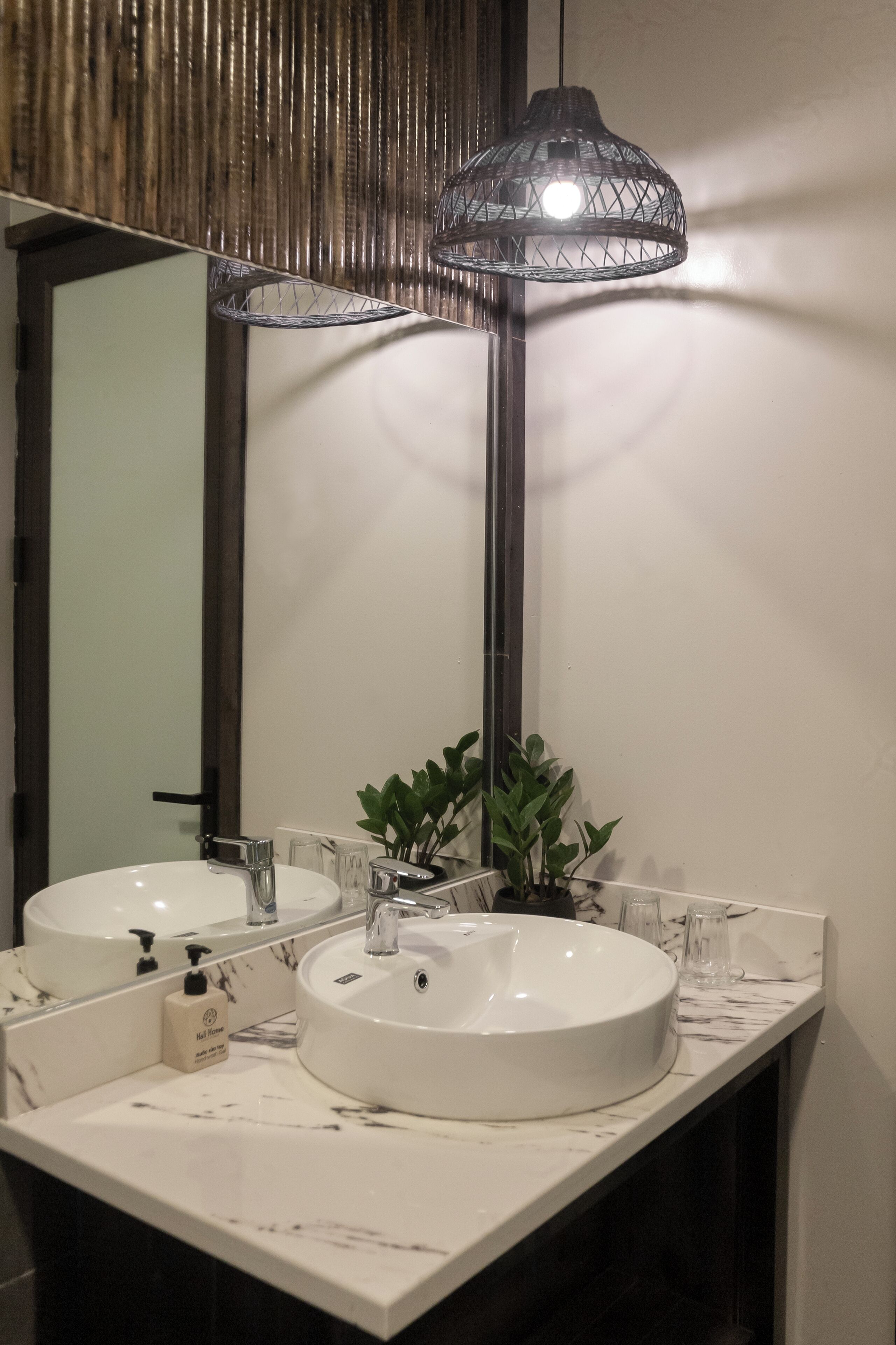 A bathroom with two sinks, a mirror, a hanging light fixture, and a potted plant.
