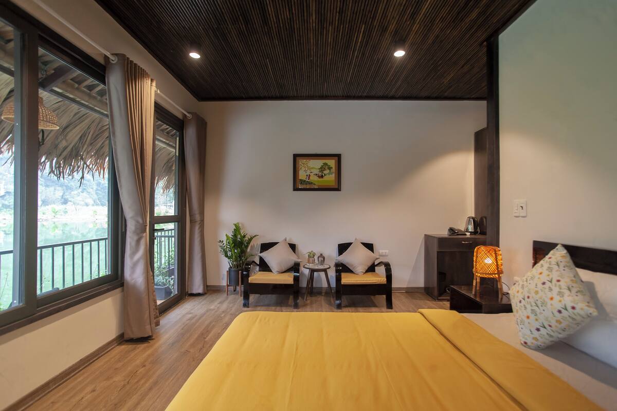 Una habitación con una cama, dos sillones, una mesita, una planta en maceta y un cuadro en la pared.