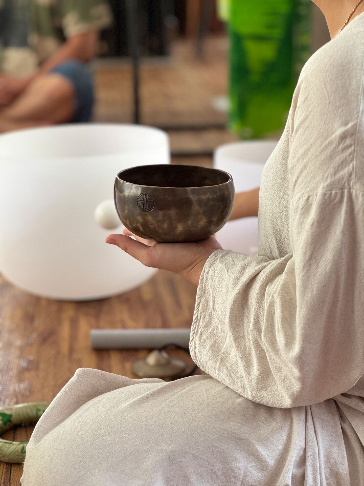 A person holding a dark-colored bowl, seated at a table with a white bowl and a green object in the background.