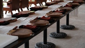 Une longue table, recouverte de planches à découper en bois et de serviettes en tissu, installée à l’extérieur sous une tonnelle.