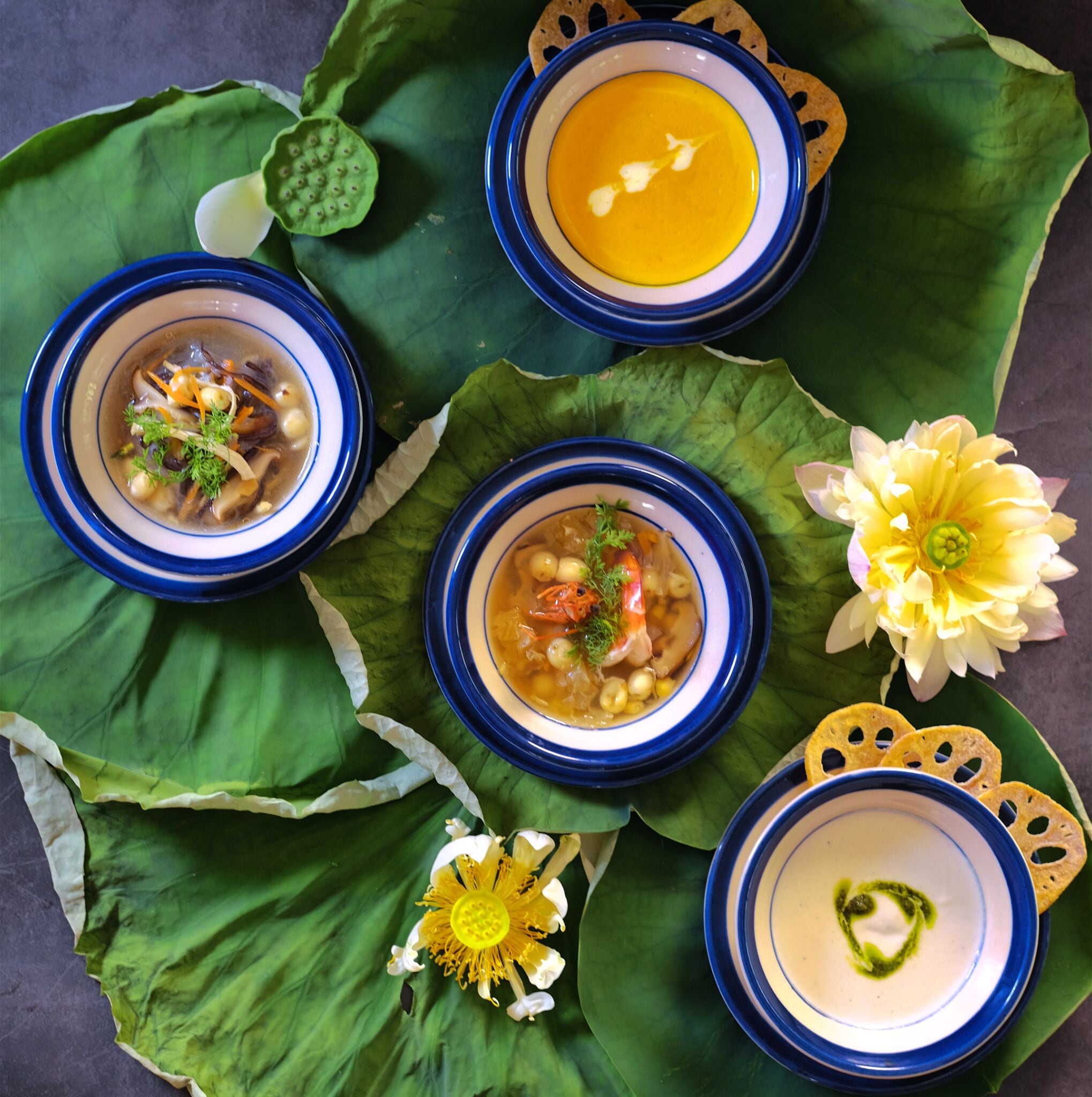 Quatre bols de soupe disposés sur une feuille verte, avec une fleur.