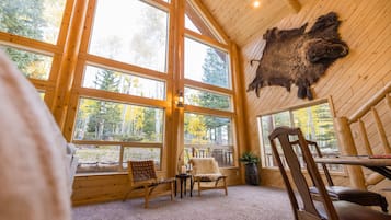 A log cabin interior with large windows, a mounted buffalo hide, and a cozy seating area.