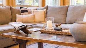 Un salon chaleureux avec une table basse en bois, un canapé agrémenté de coussins, une bougie allumée et un vase.