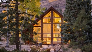 Une cabane en rondins dotée de nombreuses grandes fenêtres, d’une terrasse et de meubles pour s’asseoir à l’extérieur.