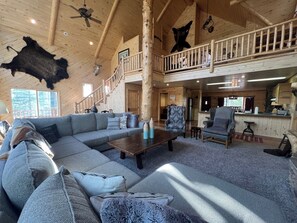 Relax in a cozy cabin-style retreat with a spacious living area, L-shaped sofa, and balcony overlooking a deck.