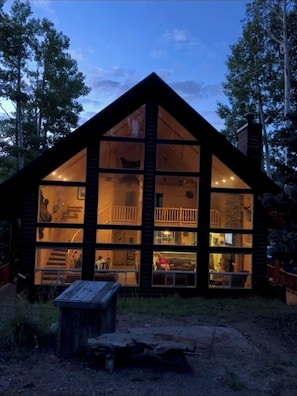 Cozy cabin with a fireplace and large windows offering a serene forest view.