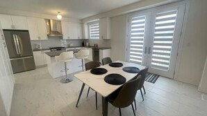 Eine moderne Küche mit weißen Schränken, einem Edelstahl-Kühlschrank, einem Gasherd und einem Essbereich mit Tisch und Stühlen.
