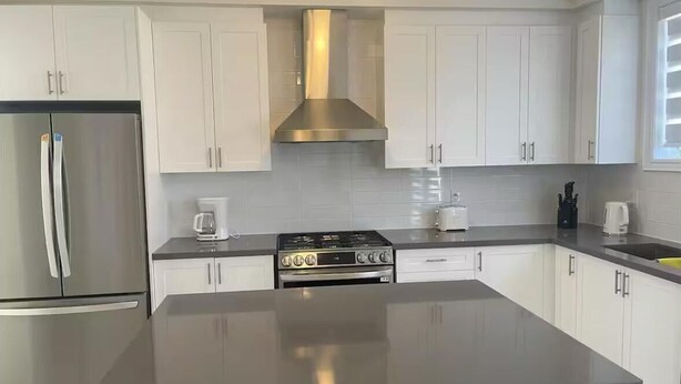 Eine moderne Küche mit weißen Schränken, einem Edelstahlkühlschrank, einem Gasherd und einer großen Kochinsel.