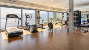 A modern gym with cardio equipment, weight machines, and large windows offering a view of a lake.