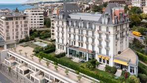 A multi-story hotel with a central courtyard, large windows, and a view of the sea.