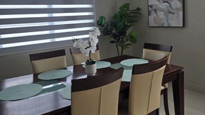 Un coin repas avec une table en bois foncé, des chaises de couleur beige et une orchidée blanche dans un vase.