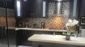 Une cuisine moderne avec des meubles de couleur sombre, un réfrigérateur en acier inoxydable, une machine à café et une petite plante en pot posée sur l’îlot central.
