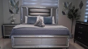 Une chambre moderne avec un grand lit, une table de chevet, une commode et une fenêtre avec des stores.