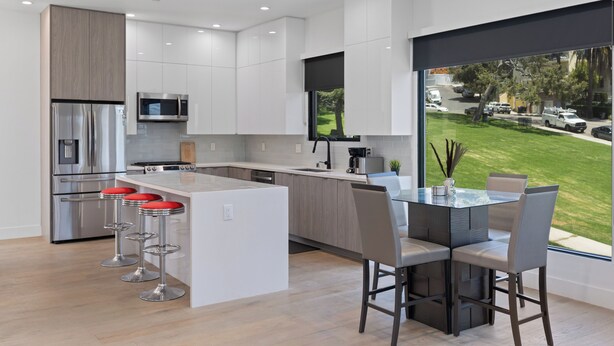 A modern kitchen with stainless steel appliances, a central island with bar stools, and a view of a green landscape through large windows. - Stylish Modern Home, Private Rooftop & City Views! (Los Angeles)