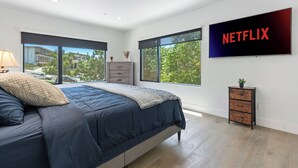 A modern bedroom with a large bed, a TV mounted on the wall, and a view of the outside through large windows. - Stylish Modern Home, Private Rooftop & City Views! (Los Angeles)