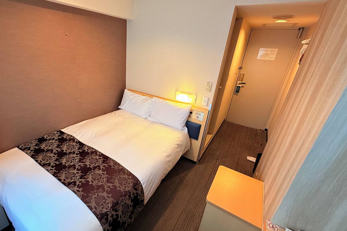 A hotel room with a bed, a nightstand, a lamp, and a door leading to a bathroom.