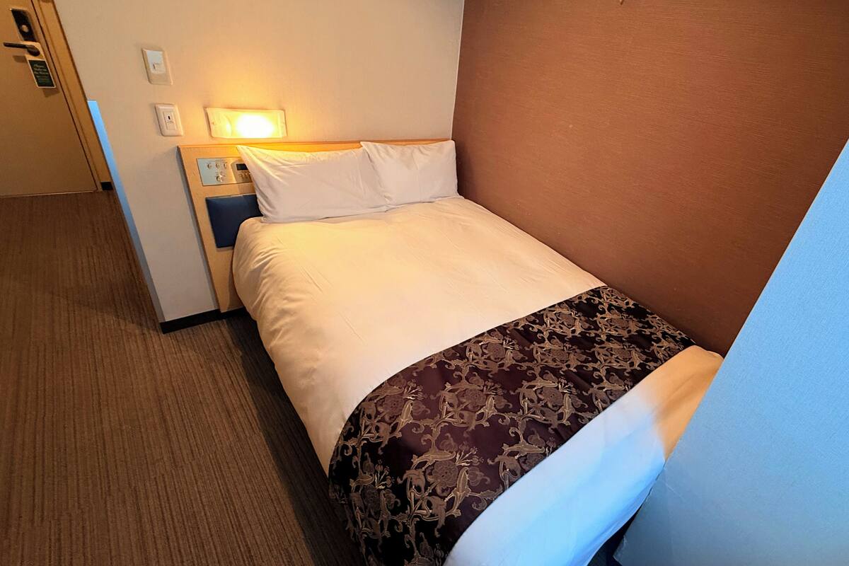 A hotel room with a bed, a nightstand, a lamp, and a door.