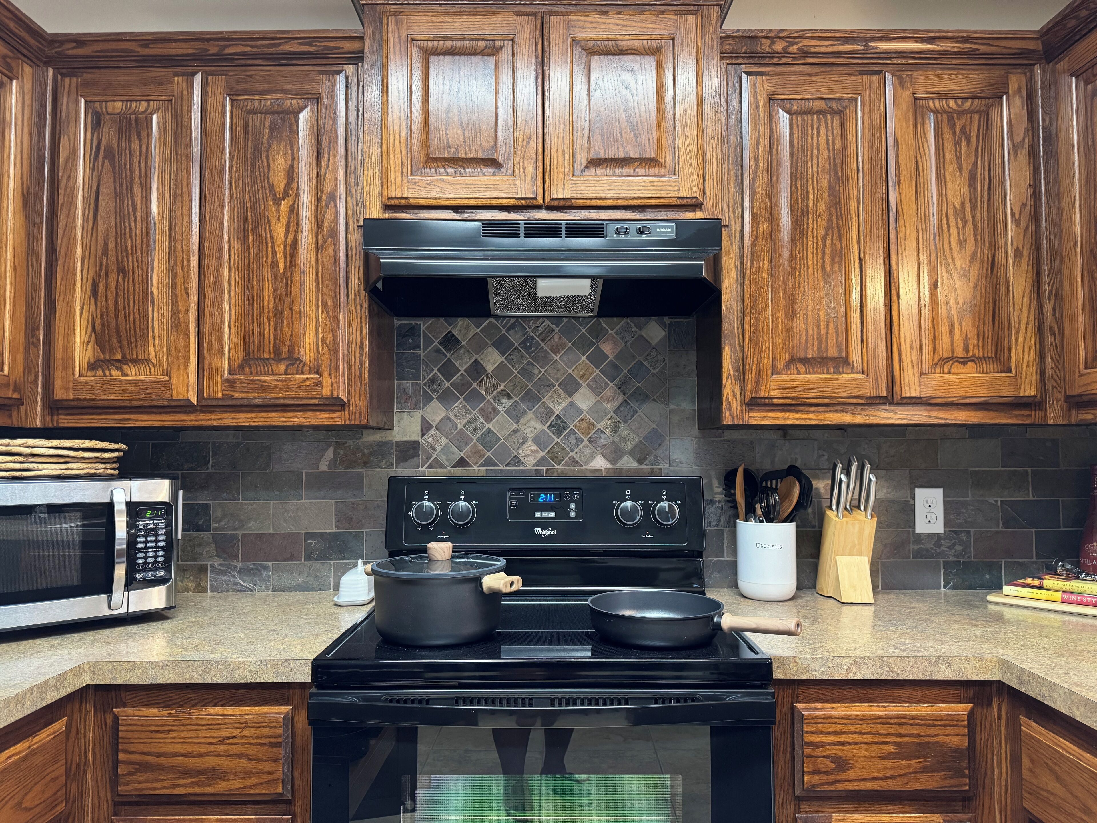A kitchen with wooden cabinets, a black stove, a microwave, and a tiled backsplash.