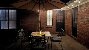Eine Terrasse im Freien mit Tisch, Stühlen und einem großen Sonnenschirm, an einer Ziegelwand.