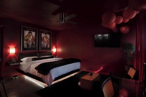 Een schemerige kamer met een bed, twee aan de muur bevestigde schilderijen, een flatscreen-tv, een plafondventilator en rode papieren lantaarns.