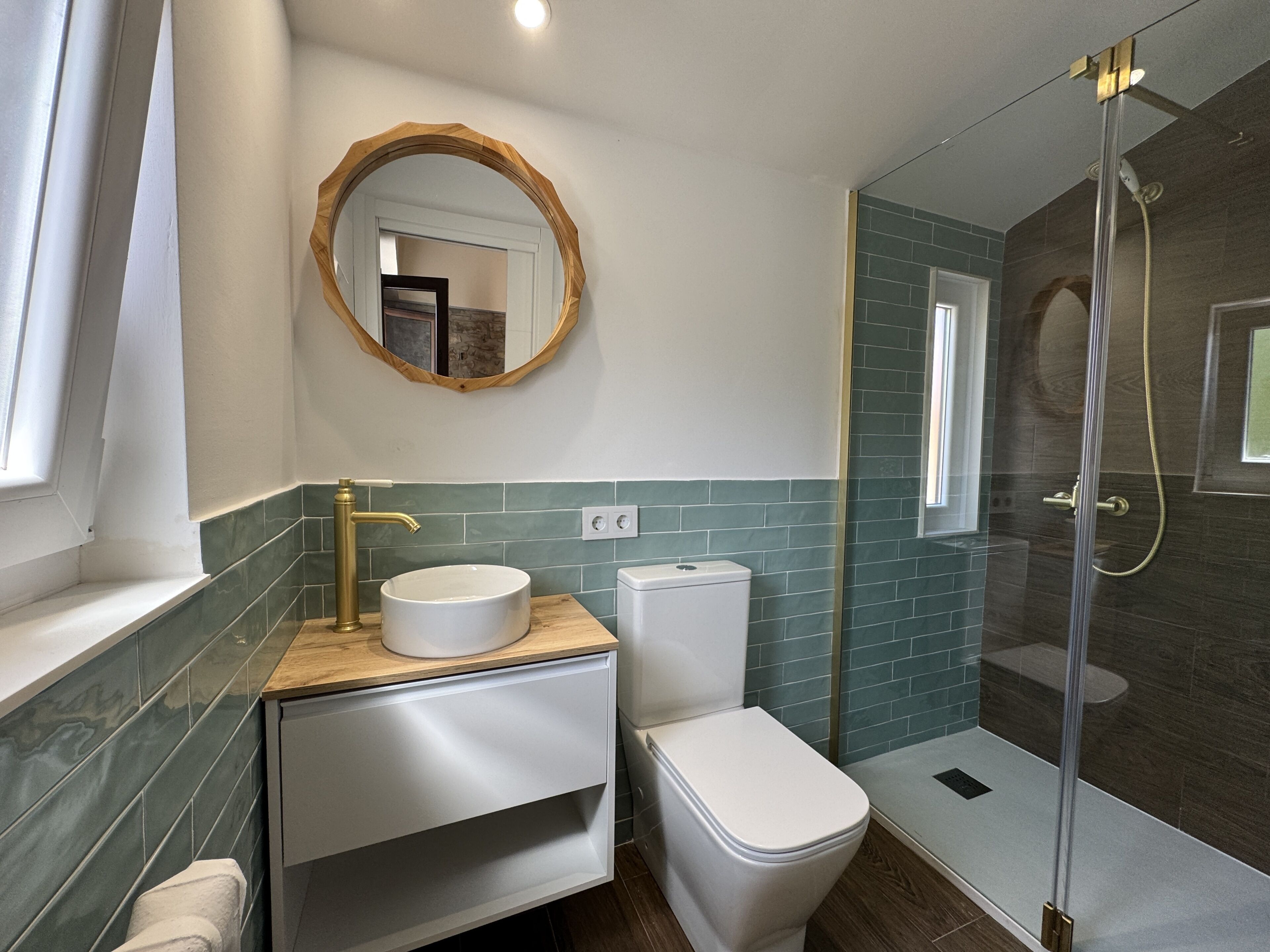 A modern bathroom with a round mirror, a white sink, a toilet, and a glass-enclosed shower area.