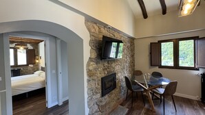 A modern interior with a stone accent wall, a fireplace, a dining area with chairs, and a bed in the adjacent room. - La Melera - Starlight lodging and skiing (Llanos)