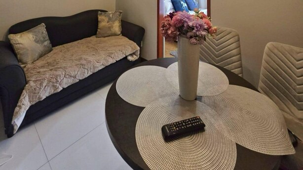 Un salon moderne avec un plafond en bois, une table basse ronde dotée d’une télécommande, un canapé et un vase décoratif rempli de fleurs.