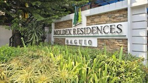 Un panneau indiquant l’emplacement de la résidence Moldex à Baguio, avec une façade en pierre et une végétation luxuriante.