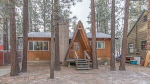 A cabin with a triangular roof, wooden exterior, and a staircase leading to the entrance.