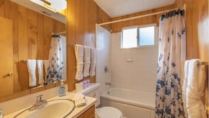 A bathroom with wooden walls, a white sink, a toilet, and a bathtub.