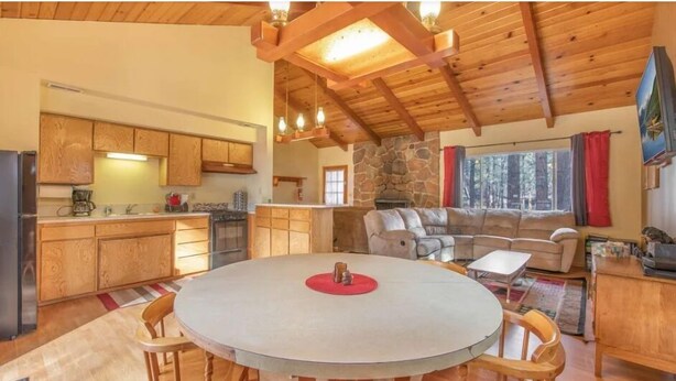 A cozy cabin interior with a stone fireplace, wooden dining table, and a large sofa.